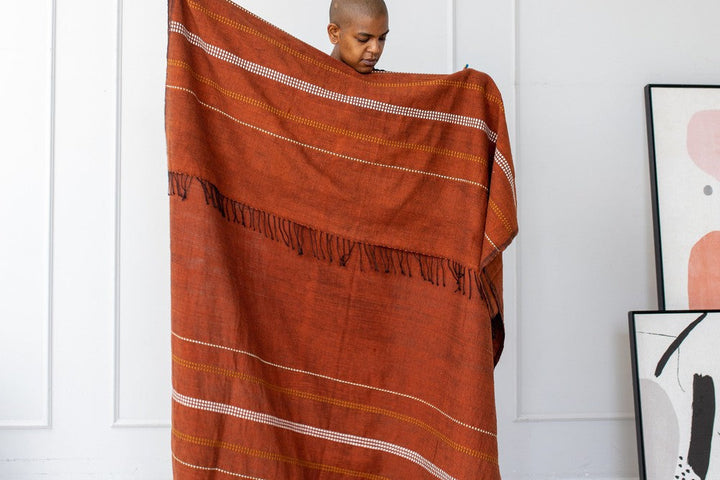Person holding the copper cotton throw open against a white wall.