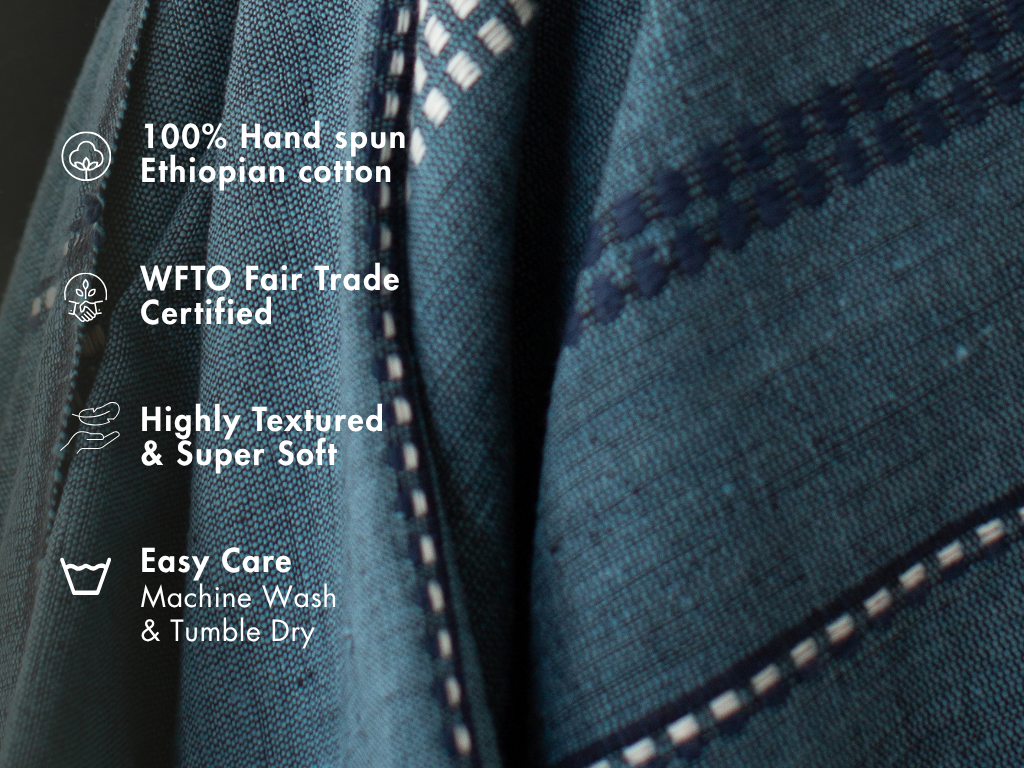 Steel blue cotton throw close-up with notes: 100% hand-spun Ethiopian cotton, WFTO Fair Trade certified, highly textured and soft, machine wash and tumble dry.