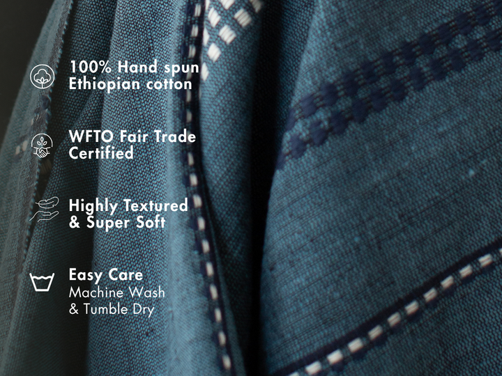 Steel blue cotton throw close-up with notes: 100% hand-spun Ethiopian cotton, WFTO Fair Trade certified, highly textured and soft, machine wash and tumble dry.